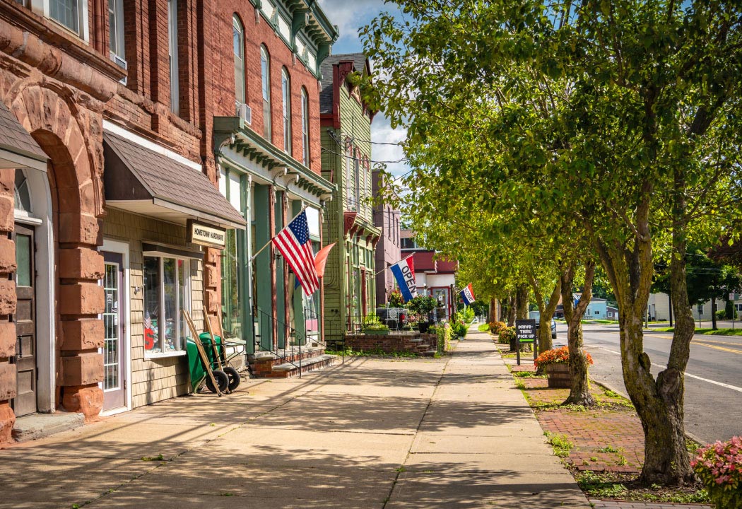looking down a shop-lined street with trees and an american flag